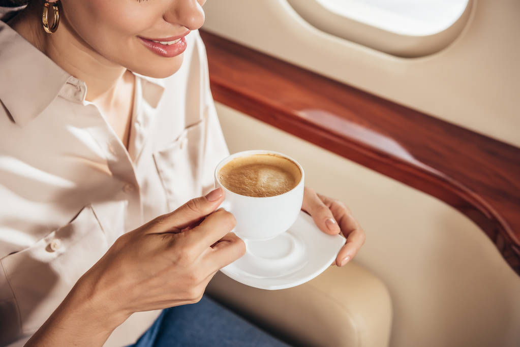 Özel uçakta elinde kahve fincanı tutan tişörtlü, gülümseyen bir kadın görüntüsü.  - Fotoğraf, Görsel