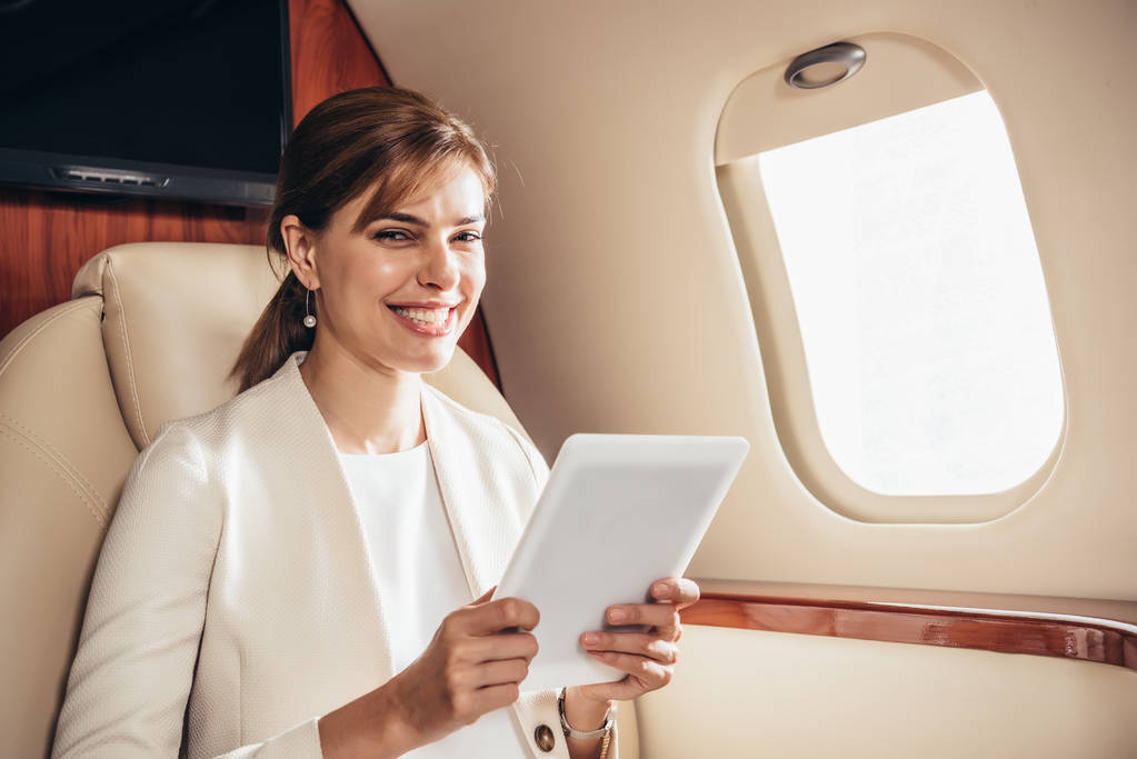 χαμογελαστή επιχειρηματίας με κοστούμι χρησιμοποιώντας ψηφιακή ταμπλέτα σε ιδιωτικό αεροπλάνο  - Φωτογραφία, εικόνα