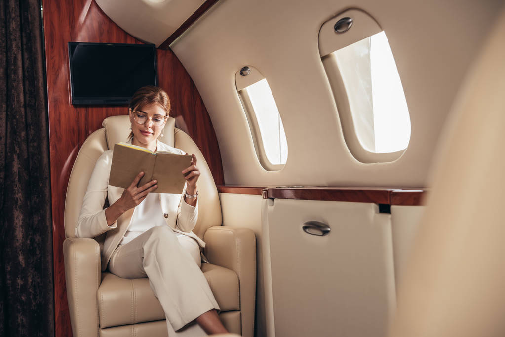 スーツ姿の魅力的な実業家が民間航空機で本を読んで  - 写真・画像