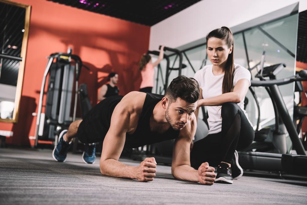 attractive trainer supervising sportsman doing plank exercise - Photo, Image