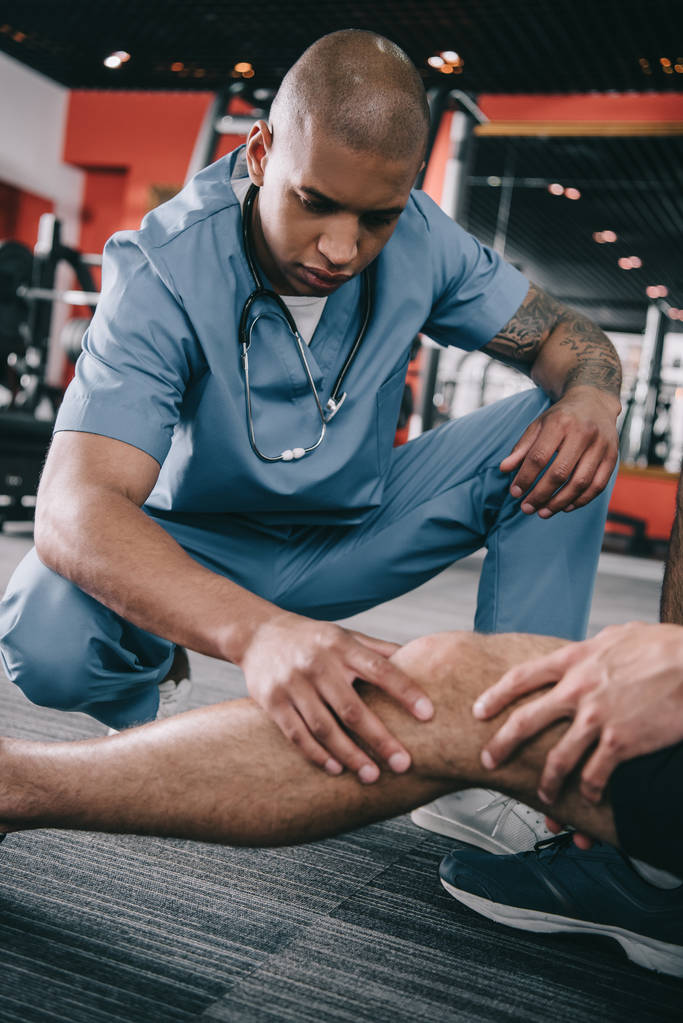 grave médico afro-americano examinando joelho ferido de desportista
  - Foto, Imagem