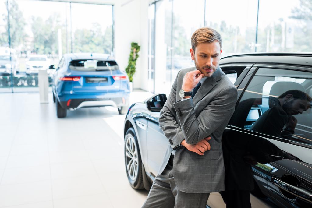 столярний бородатий бізнесмен стоїть біля автомобілів в автосалоні
  - Фото, зображення