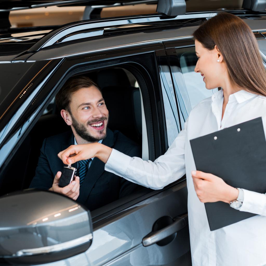 Selektiver Fokus der attraktiven Frau, die dem glücklichen Mann im Auto den Autoschlüssel gibt  - Foto, Bild