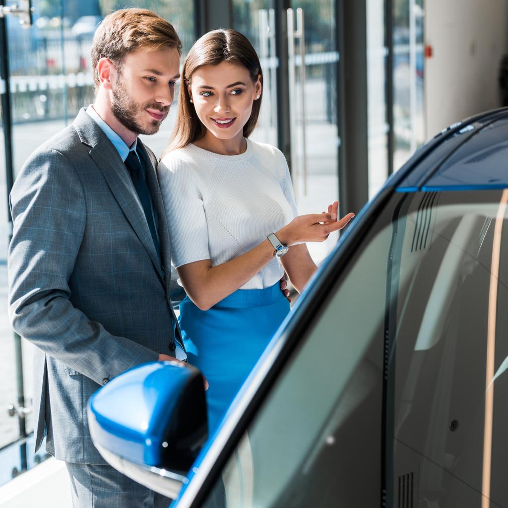 επιλεκτική εστίαση της όμορφης γυναίκας gesturing, ενώ στέκεται με όμορφο άνδρα και μπλε αυτοκίνητο  - Φωτογραφία, εικόνα