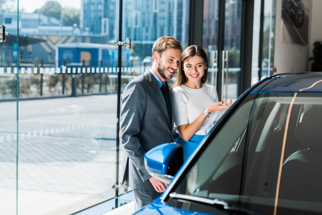 selektywne skupienie pięknej dziewczyny gestykulując stojąc z przystojnym mężczyzną i niebieskim samochodem  - Zdjęcie, obraz