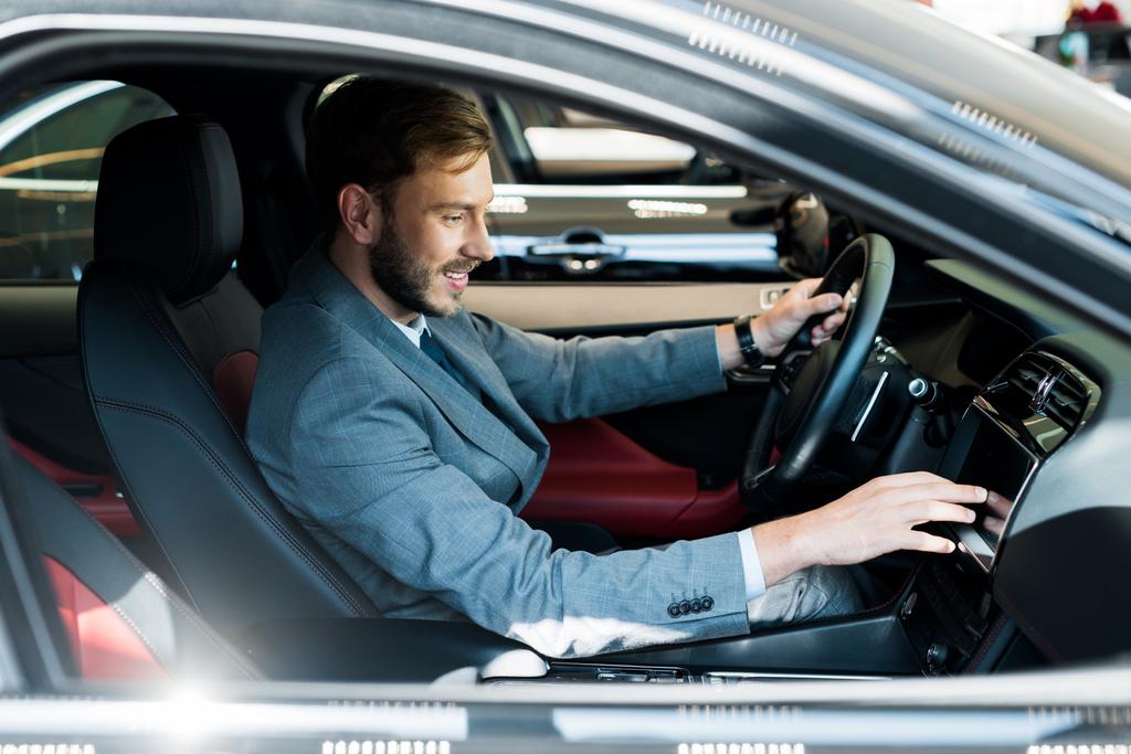 Mutlu sakallı sürücünün seçici odak noktası arabada oturmak ve dokunmak  - Fotoğraf, Görsel