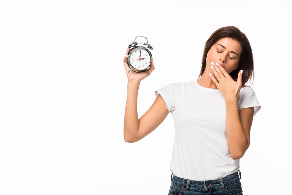 mujer cansada bostezando y sosteniendo el reloj despertador, aislado en blanco
 - Foto, Imagen
