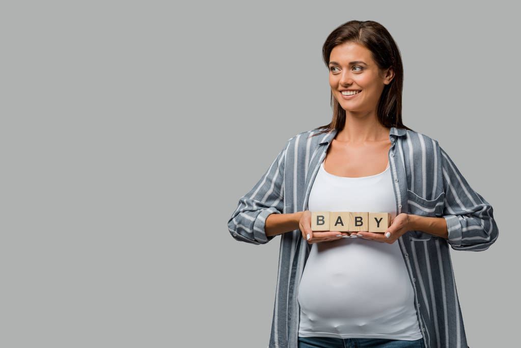 жизнерадостная беременная женщина с кубиками алфавита с детским знаком, изолированная на сером
 - Фото, изображение