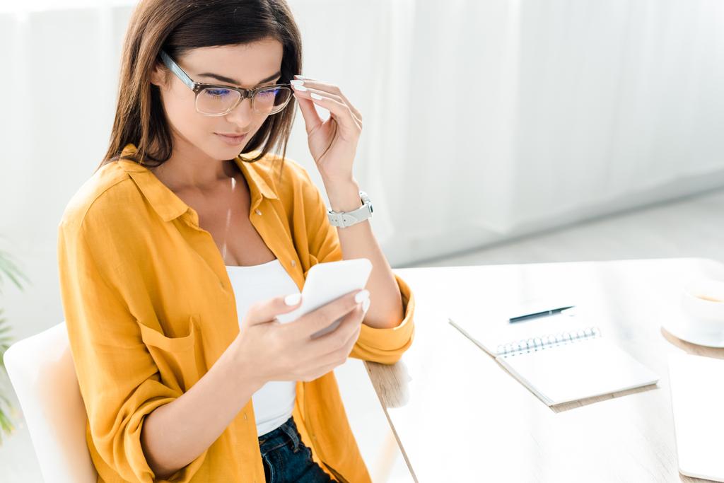 attrayant pigiste dans les lunettes en utilisant smartphone dans le bureau à domicile
 - Photo, image
