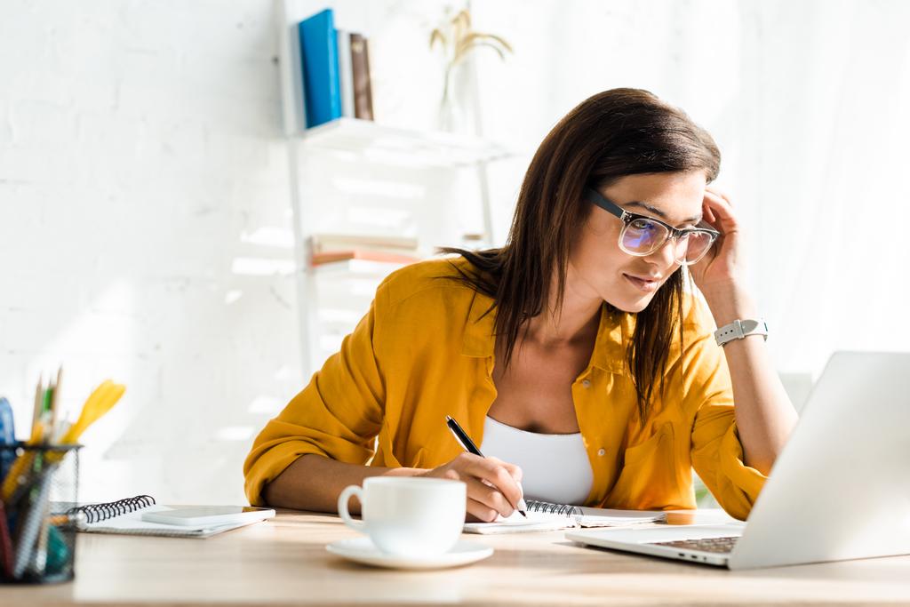 atraktivní žena na volné noze pracující na notebooku a psaní v domácí kanceláři - Fotografie, Obrázek