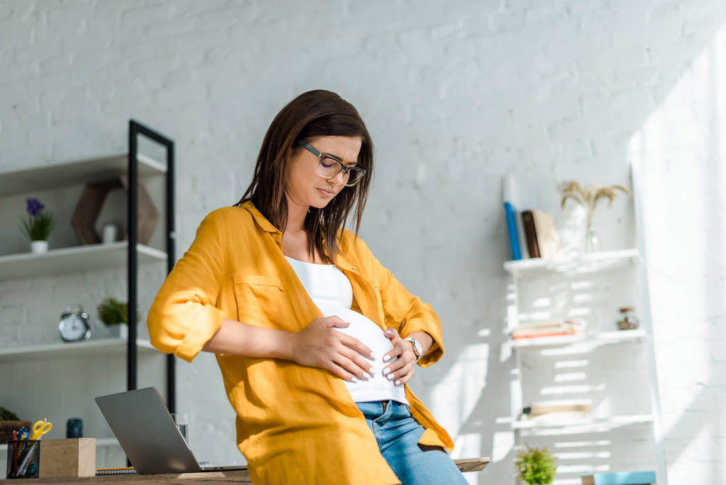 schöne müde schwangere Freiberuflerin mit Bauchschmerzen im Home Office - Foto, Bild