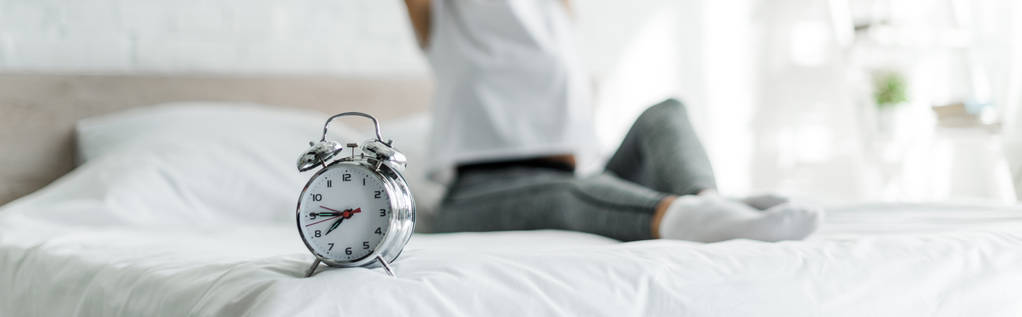 cropped view of woman sitting with alarm clock on bed - Photo, Image