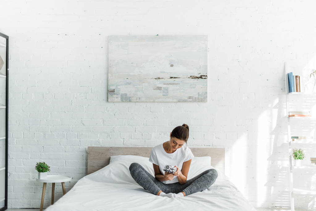 счастливая девушка, сидящая с будильником на кровати по утрам
 - Фото, изображение
