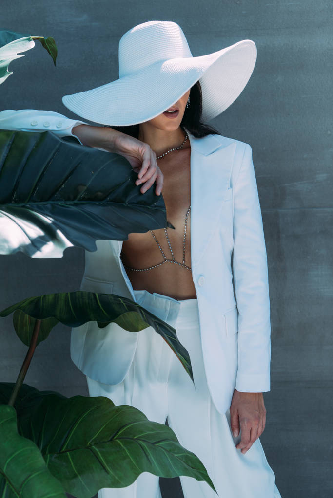 Nainen valkoisessa puvussa ja hattu poseeraa ja pitää lomaa ulkona
  - Valokuva, kuva