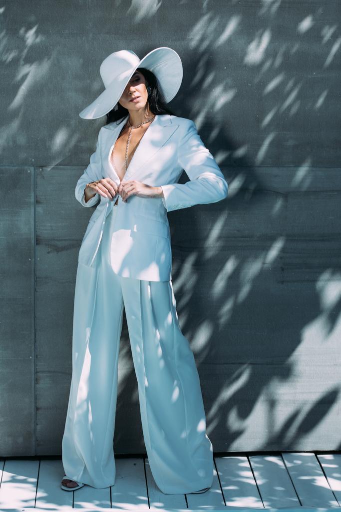 atractiva mujer en traje blanco y sombrero posando y mirando hacia afuera
  - Foto, Imagen