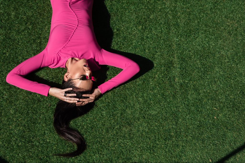top view of attractive woman in dress and sunglasses posing and lying on grass outside  - Photo, Image