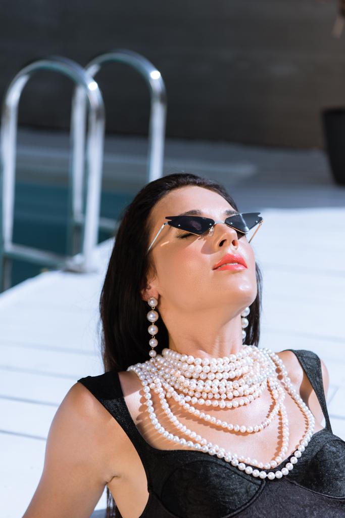 Siyah mayolu ve güneş gözlüklü çekici kadın dışarıda poz veriyor.  - Fotoğraf, Görsel