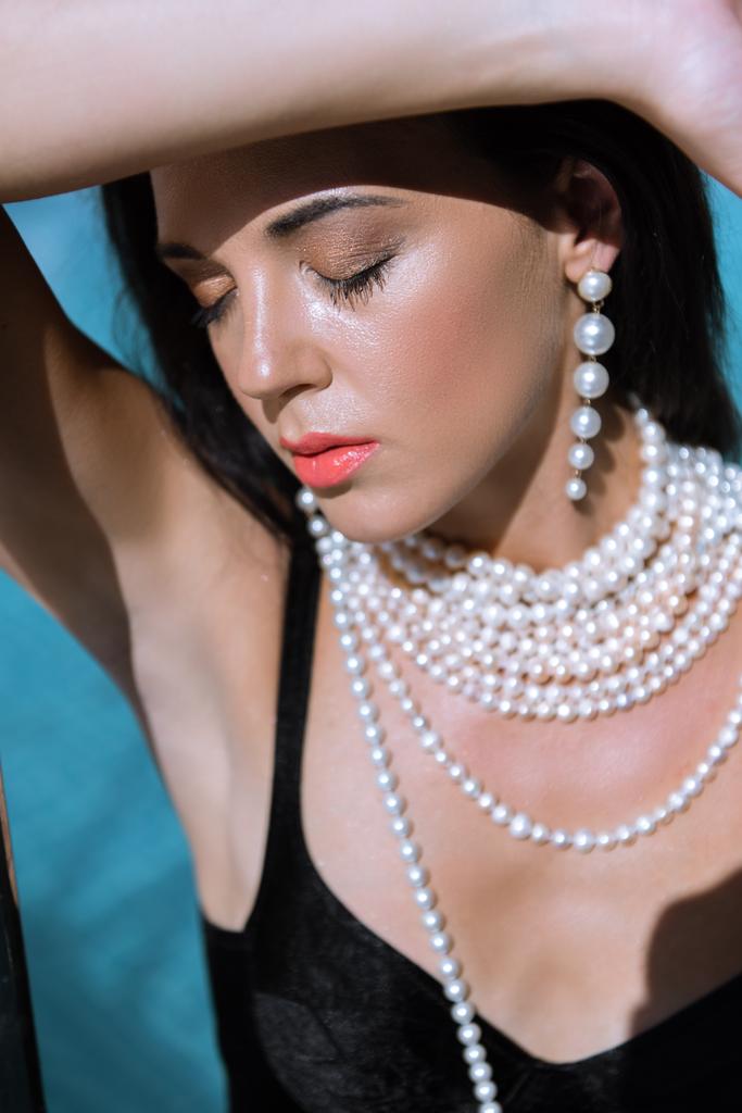 привлекательная женщина в черном купальнике и жемчужном ожерелье с закрытыми глазами
  - Фото, изображение