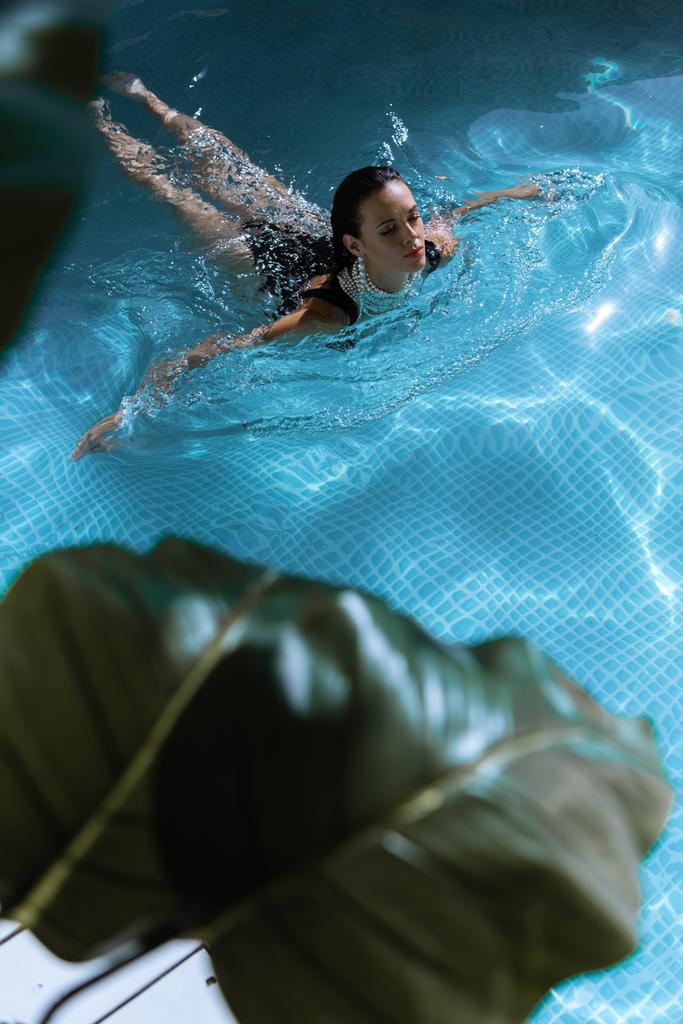 selektiver Fokus der attraktiven Frau in Perlenkette, die im Pool schwimmt  - Foto, Bild