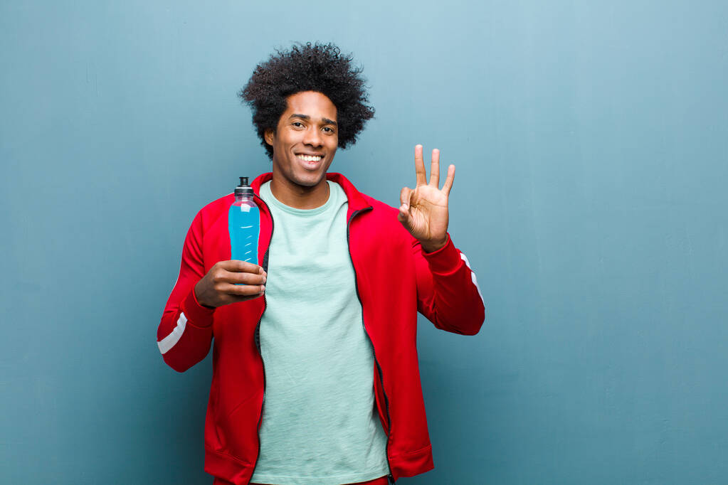 mladý černošky muž se sportovním nápojem proti modré grunge zeď - Fotografie, Obrázek