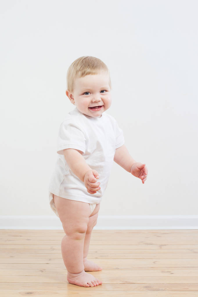 śmieszne małe dziecko stawia pierwsze kroki na drewnianej podłodze - Zdjęcie, obraz