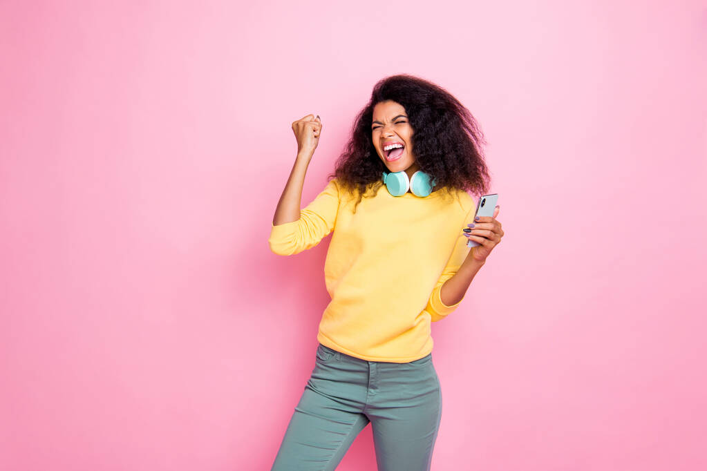 Retrato de loco funky hipster africano chica uso celular obtener retroalimentación de seguidores levantar puños grito sí celebrar logro desgaste amarillo suéter pantalones aislados sobre rosa color de fondo
 - Foto, Imagen