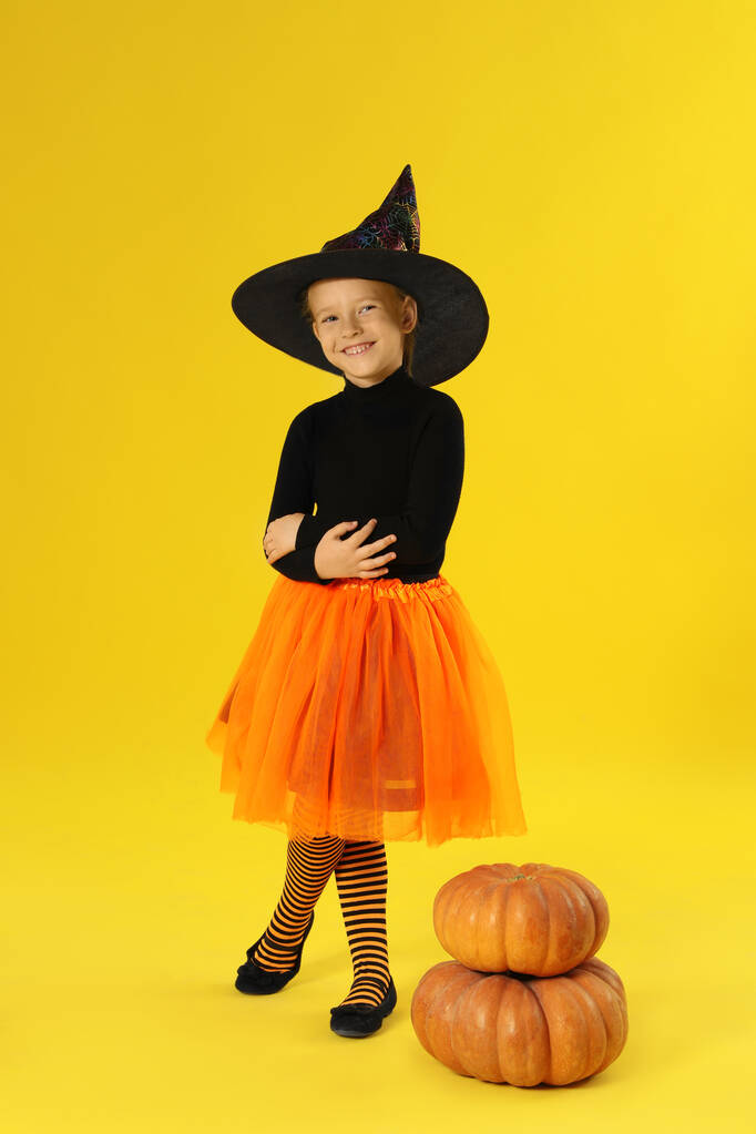 Schattig klein meisje met pompoenen dragen Halloween kostuum op gele achtergrond - Foto, afbeelding