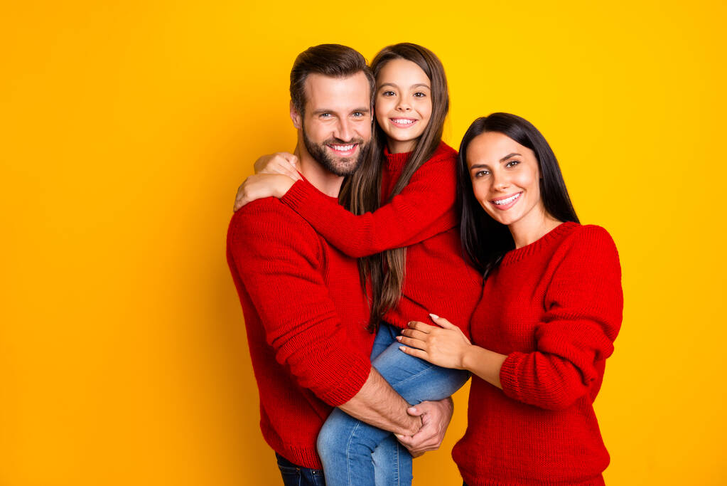 Фото забавного дня зубастая милая очаровательная семья с ребенком в джинсах джинсы красный свитер отец держа дочь с руками мать объятия изолированы на ярком цветном фоне
 - Фото, изображение