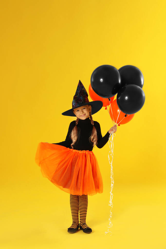 Sarı arka planda Cadılar Bayramı kostümü giyen balonlu şirin küçük kız. - Fotoğraf, Görsel