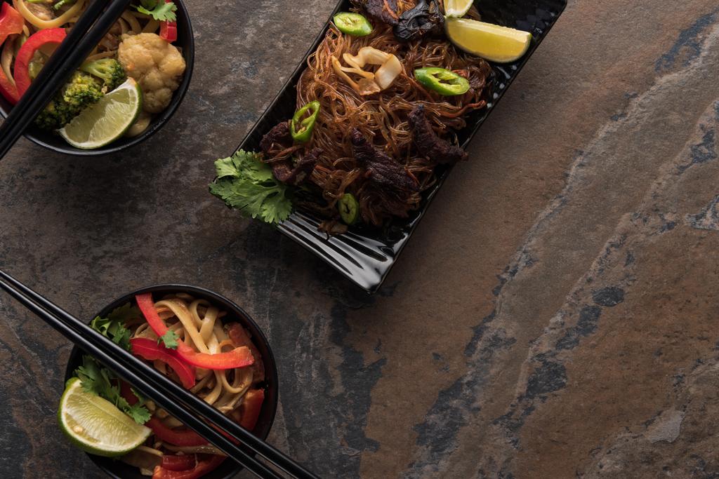 вид сверху на вкусную пряную тайскую лапшу с палочками для еды на каменной поверхности
 - Фото, изображение