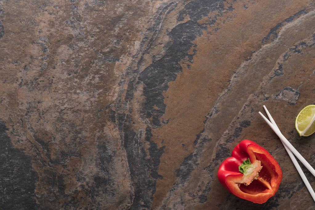 bovenaanzicht van paprika, limoen, eetstokjes op stenen ondergrond - Foto, afbeelding