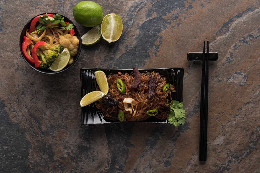 вид сверху на вкусную пряную тайскую лапшу с палочками для еды на каменной поверхности
 - Фото, изображение