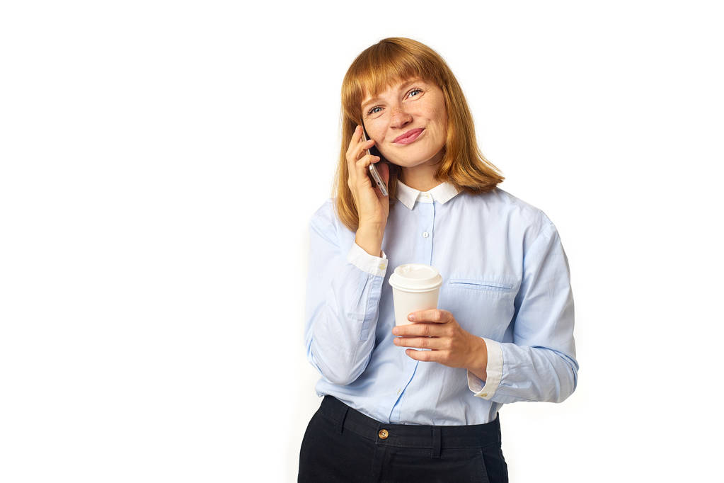 joven pelirroja mujer con pecas y bang hablando por teléfono y sonriendo mientras sostiene la taza de café en la mano
  - Foto, imagen