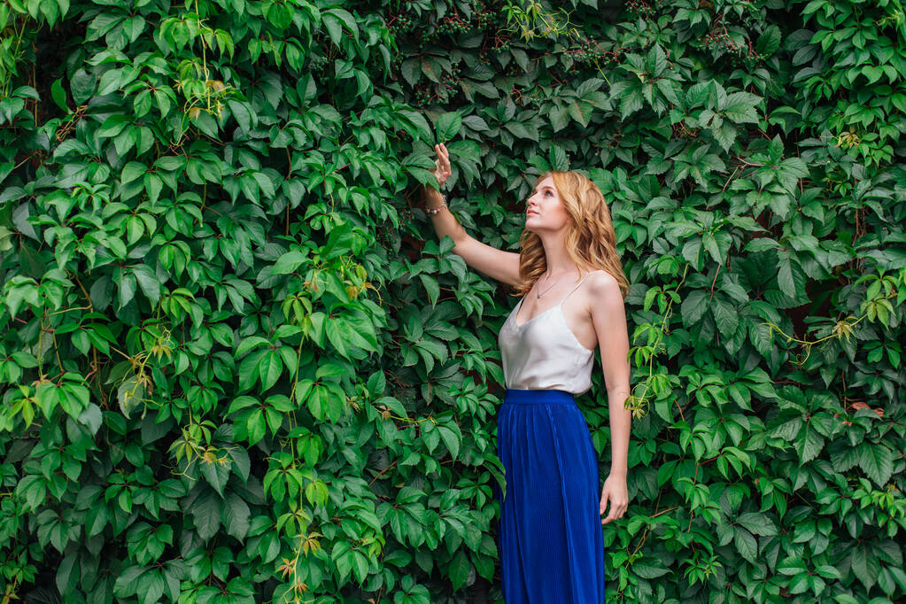 Porträt einer jungen schönen Frau, die neben der Wand aus wilden Traubenblättern steht. - Foto, Bild