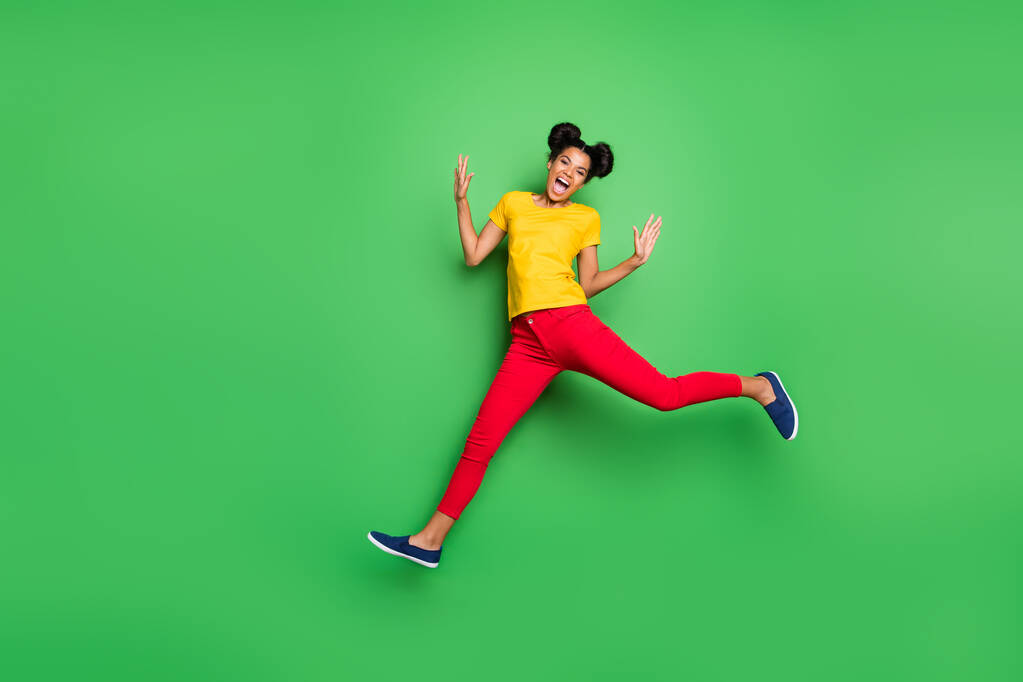 Фотографія повної довжини досить темної шкіри леді стрибає високі спортивні змагання бігун учасник одягнений в повсякденну жовту футболку червоні штани ізольовані зелений фон
 - Фото, зображення