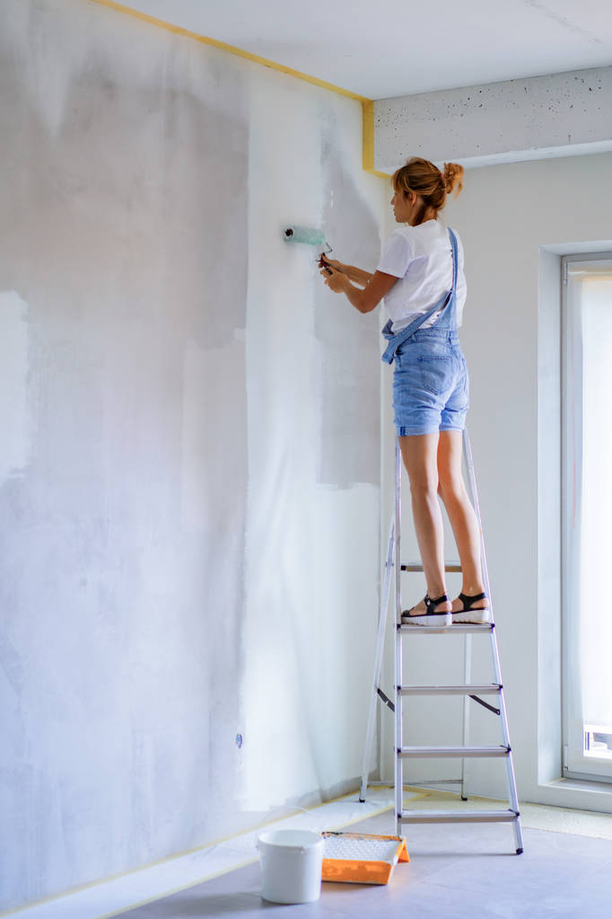 jonge mooie vrouw maakt reparaties in het appartement, schildert de muren met een roller. Molair werk. - Foto, afbeelding