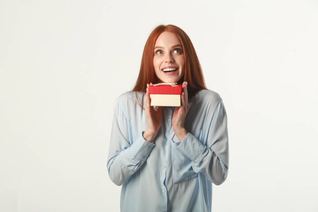 hermosa joven con el pelo rojo con un regalo sobre un fondo blanco
 - Foto, Imagen