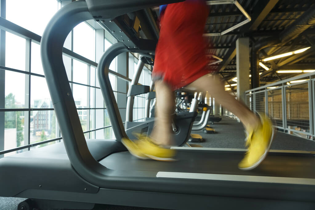 Nohy s tenisky mužského běžce. běžec běží na běžeckém pásu uvnitř v akci - s pohybem rozmazaný.Rozmazané muže nohy běží na běžícím pásu v tělocvičně - Fotografie, Obrázek