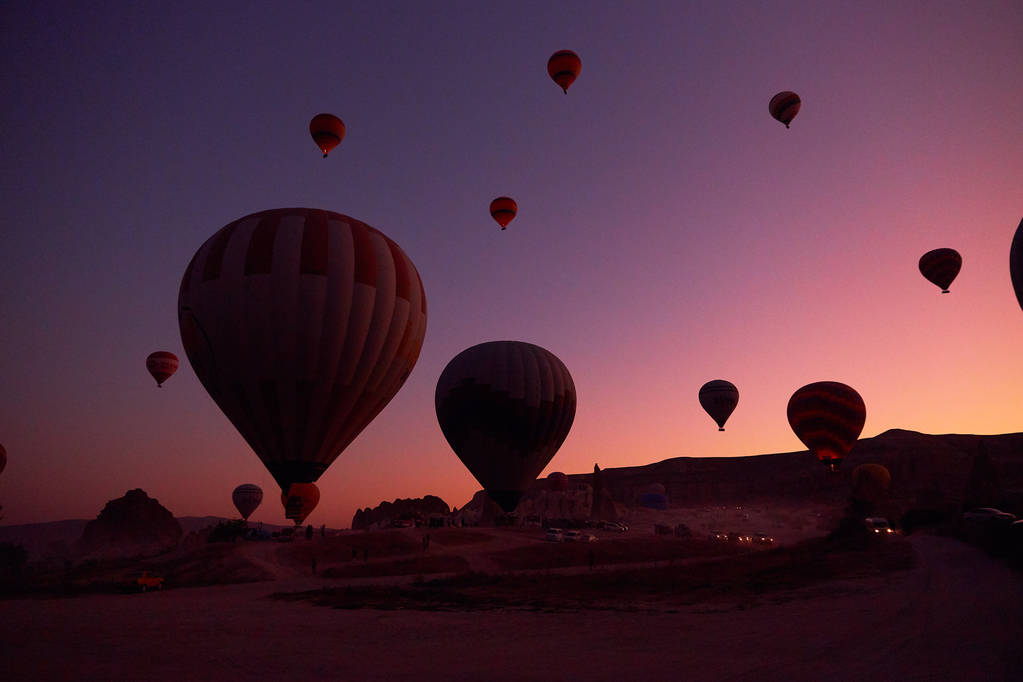 zdjęcie wschodu słońca z dużymi balonami na niebie i ludźmi i samochodami na ziemi - Zdjęcie, obraz