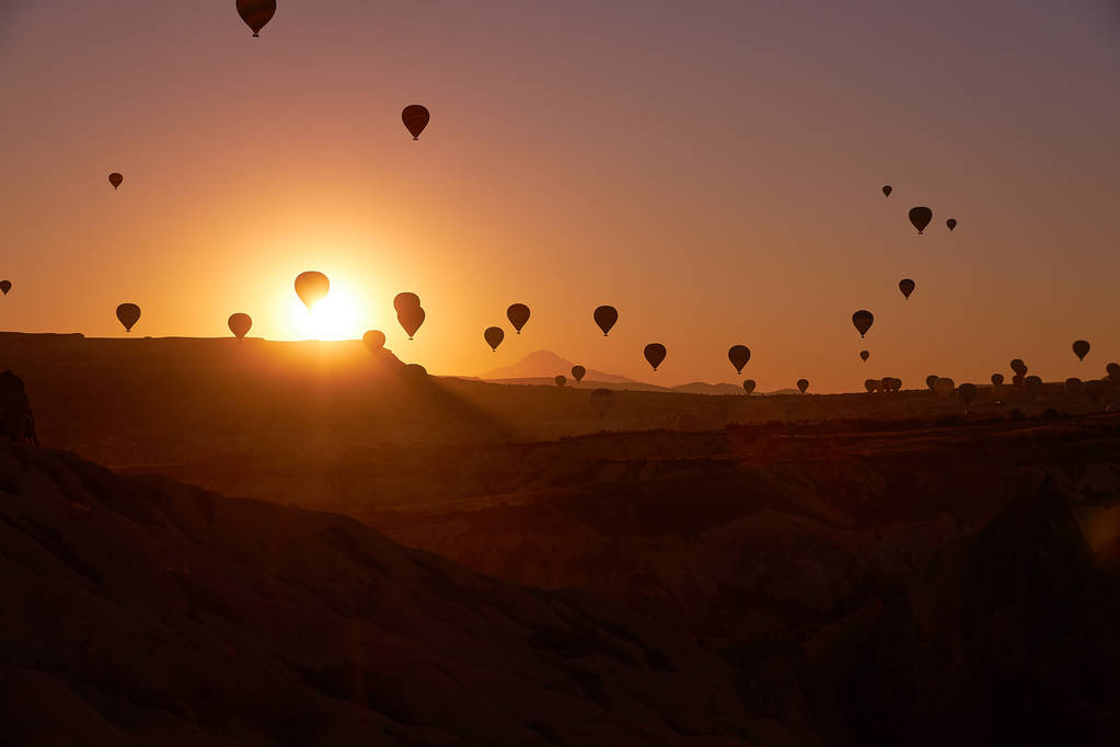 Фото сходу сонця в Каппадокії з повітряними кулями в небі над піщаними пагорбами. - Фото, зображення