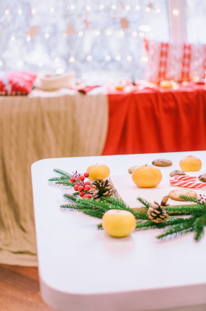 Pokój i stół urządzone na Boże Narodzenie. Świąteczny stół w pierniki ciasteczka, mleko, mandarynki i igły. Świąteczny nastrój - Zdjęcie, obraz