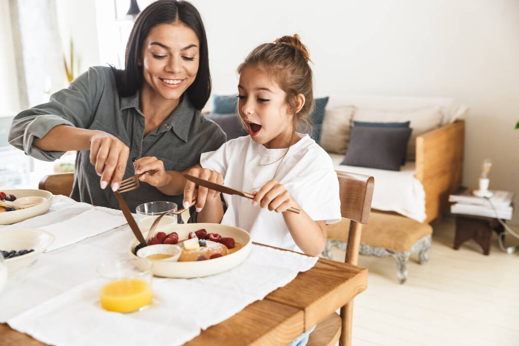 Imagen de la familia emocionada madre e hija pequeña comiendo togeth
 - Foto, imagen