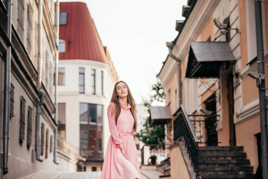 Ein junges, schönes Mädchen in einem rosafarbenen Kleid geht durch die schönen Straßen der Stadt. sehr schöne Porträts eines Mädchens in der Stadt. - Foto, Bild