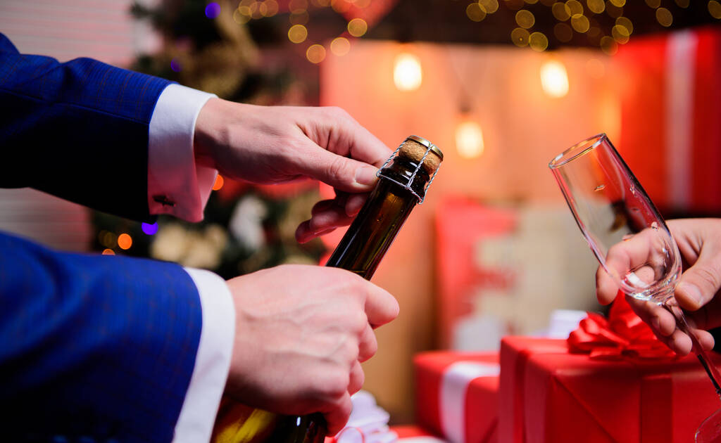 Igyál pezsgőt vagy pezsgőt. Ünnepeljük az új évet pezsgővel. Tósztot és éljenzést. Ünnepeljünk! Férfi kéz nyitó pezsgő palack öntő szemüveg karácsonyi dekorációk háttér - Fotó, kép