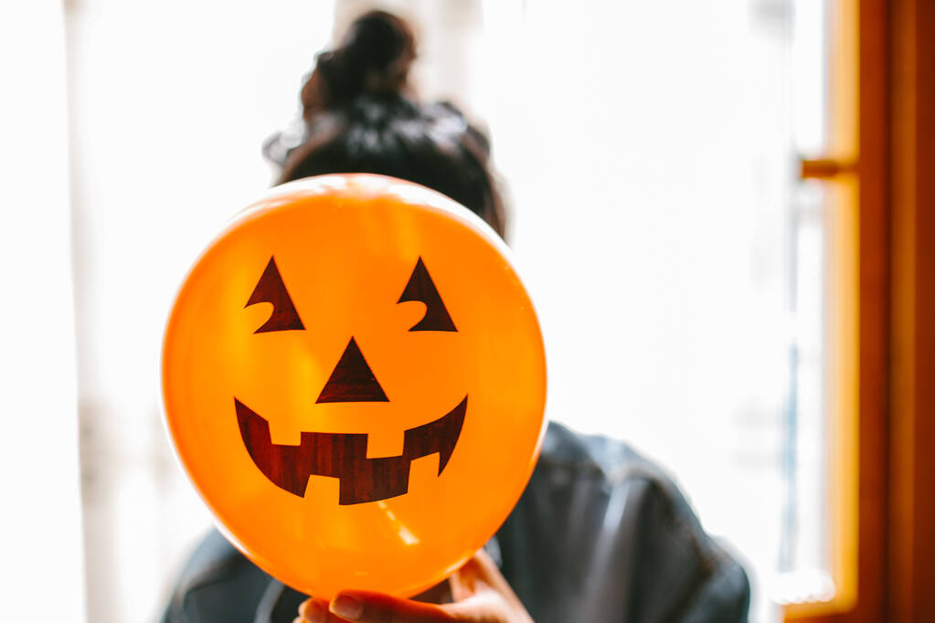 Sorcière méconnaissable tenant un ballon de citrouille avec sa main et couvrant son visage. Jeune femme célébrant Halloween. Ballons de fête à l'hélium
. - Photo, image