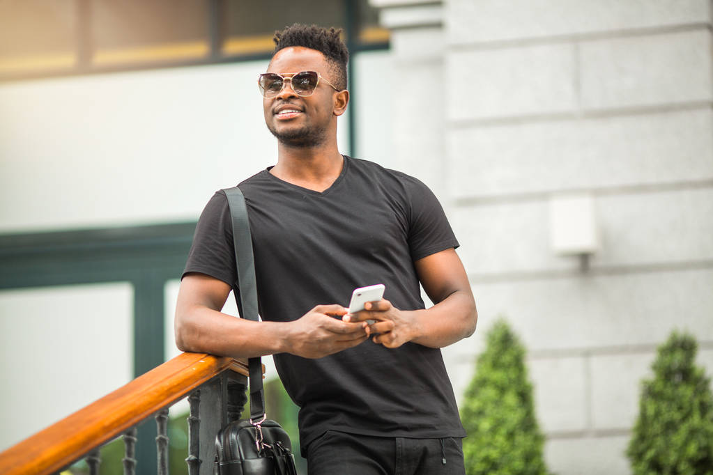 красивый молодой африканский мужчина в футболке с телефоном в руке
 - Фото, изображение