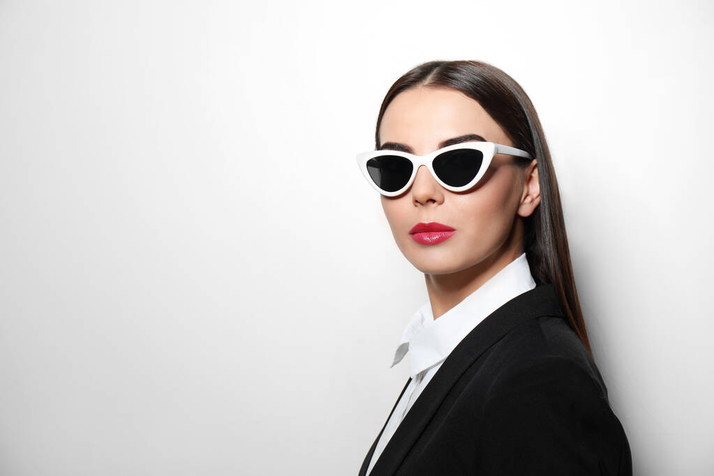 Jonge zakenvrouw in stijlvolle zonnebril op lichte achtergrond, ruimte voor tekst - Foto, afbeelding