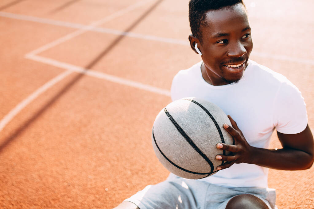 Спортивний афроамериканець відпочиває після тренування, сидячи на майданчику з баскетболістом, баскетболістом. - Фото, зображення