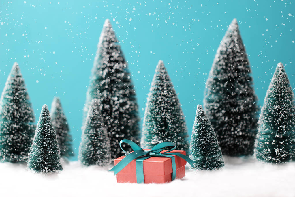 Χριστουγεννιάτικο φόντο με κόκκινο κουτί δώρου και θολή χριστουγεννιάτικα δέντρα στο τραπέζι. - Φωτογραφία, εικόνα