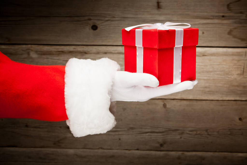 Santa hand met een rode giftdoos tegen houten achtergrond - Foto, afbeelding